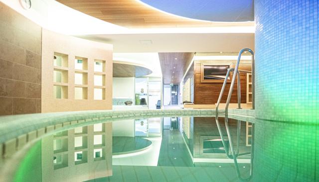 Ein stilvoll beleuchteter Innenpool mit klar schimmerndem Wasser. Sanfte Lichter spiegeln sich an den Kacheln, während eine Metallleiter ins Becken führt. Die moderne Architektur und warme Gestaltung sorgen für eine ruhige, einladende Atmosphäre.